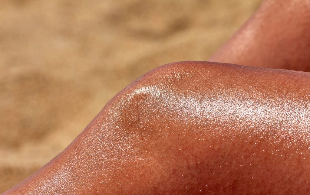 Close-up of glistening sun-kissed skin in warm summer light, highlighting skin texture and hydration.
