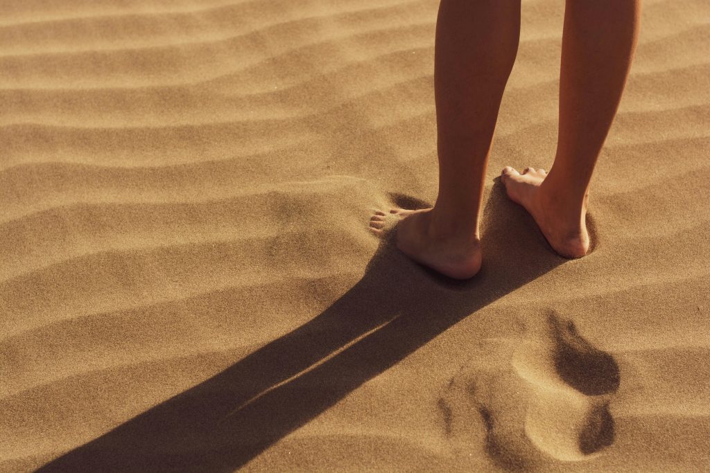 Bare feet on sunlit sand casting a shadow — symbolizing UV exposure even on cloudy days