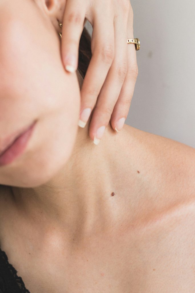 Close-up of a woman’s collarbone and neck with natural skin texture and beauty marks, hand resting gently on her neck.